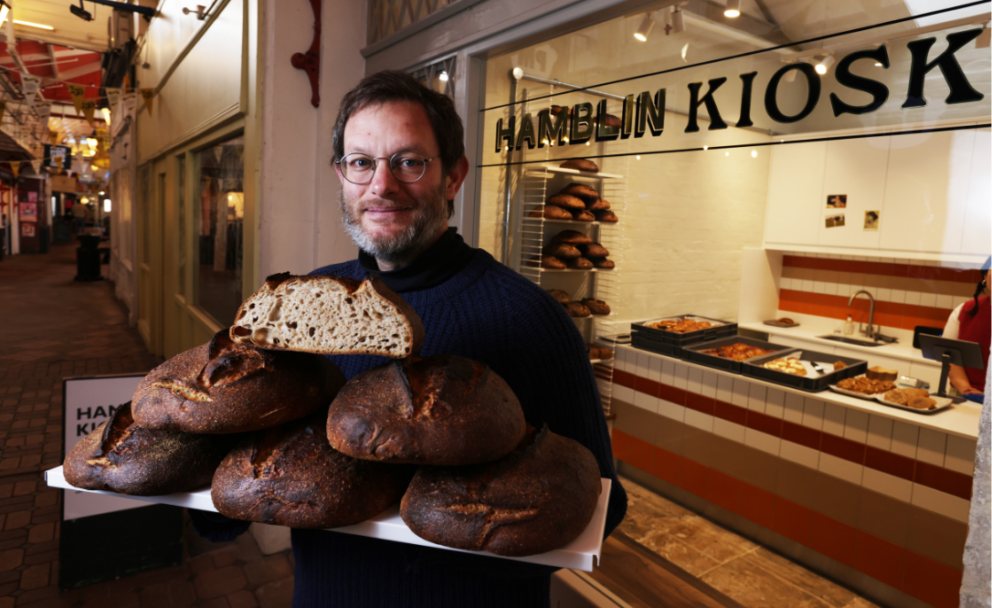 person holding tray of fresh baked loaves looking into camera