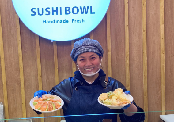 Owner Yaning is smiling to camera and holds up two bowls of sushi